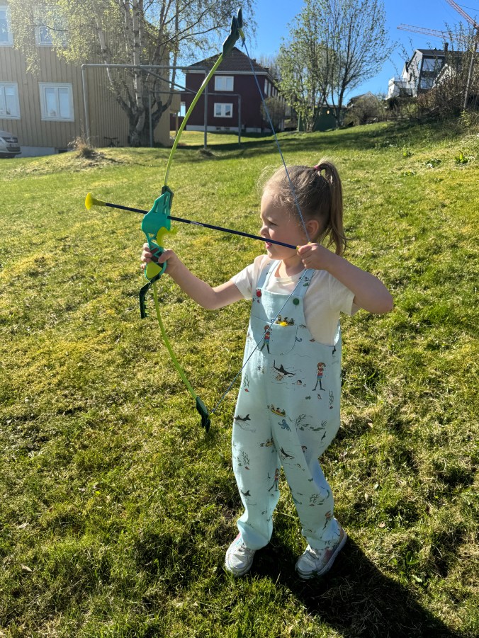 Barn i pippi-snekkerbukse skyter med pil og bue.